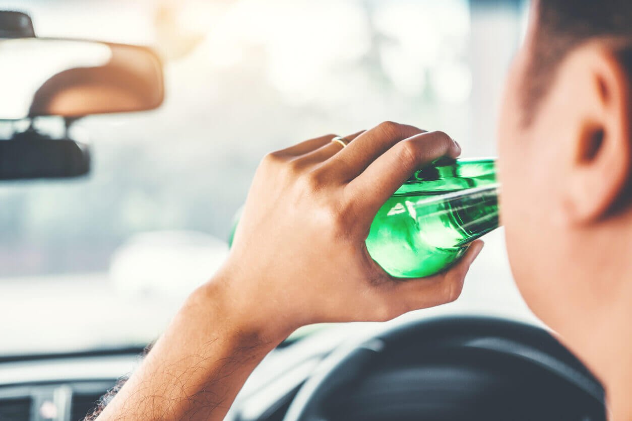 Drunk man driving a car on the road holding bottle beer Dangerous drunk driving concept